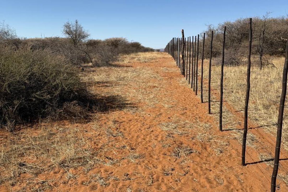 A view of an agricultural land plot featuring sandy terrain and a long stretch of wire fencing with wooden posts.