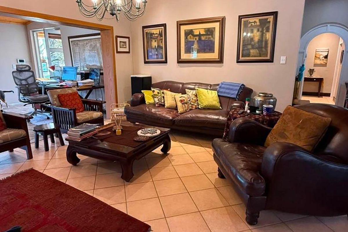 Spacious living room featuring a warm timber-clad ceiling, ceramic tiled flooring, and a classic chandelier, with an adjoining office space visible through the archway.