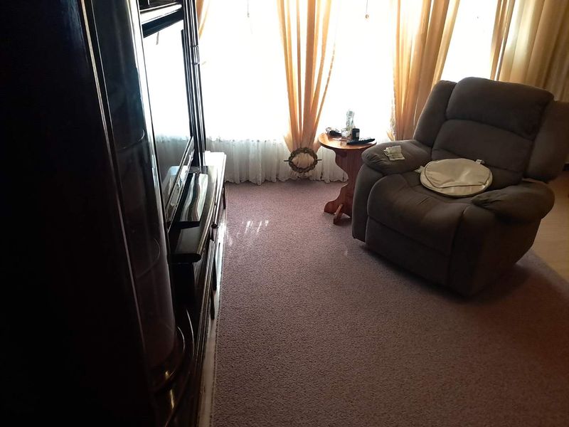 A living room area featuring carpeted flooring and a large window allowing natural light into the space.