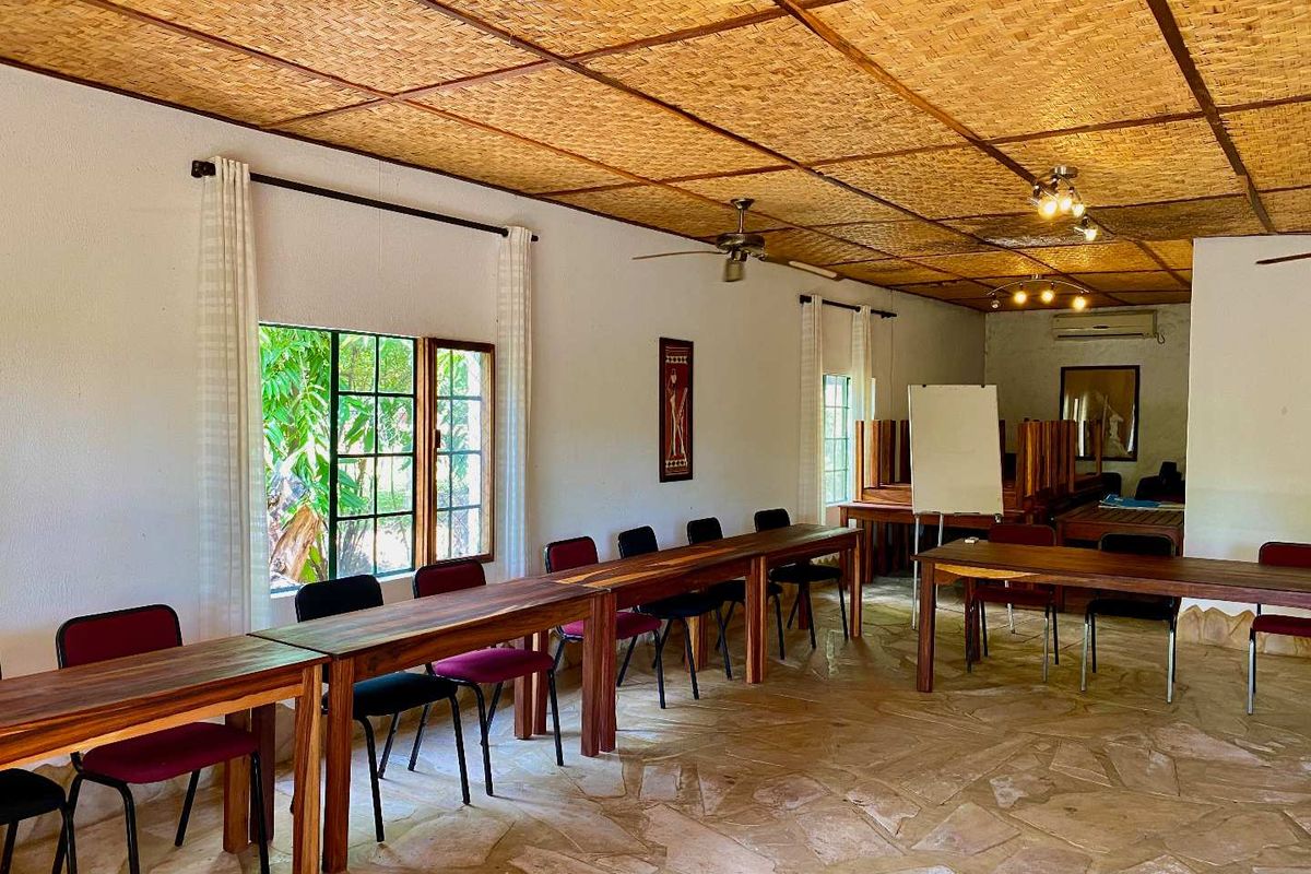 Spacious lodge meeting or dining area featuring a unique woven bamboo ceiling, stone flooring, and large windows overlooking the garden.