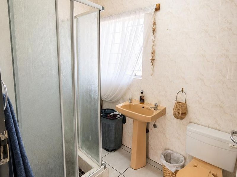 A functional bathroom featuring a shower enclosure, pedestal basin, and toilet with neutral wall and floor tiling.