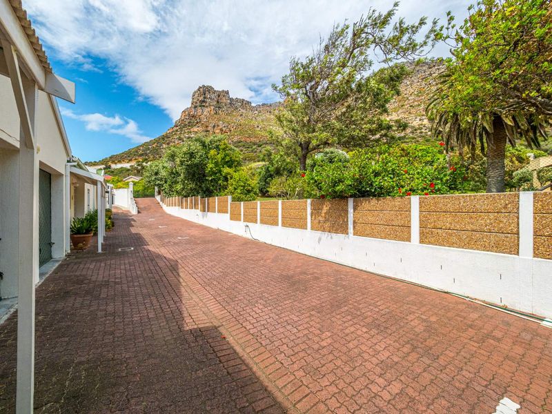 A paved driveway leading towards the townhouse garage, featuring a boundary wall and scenic mountain views in the background.