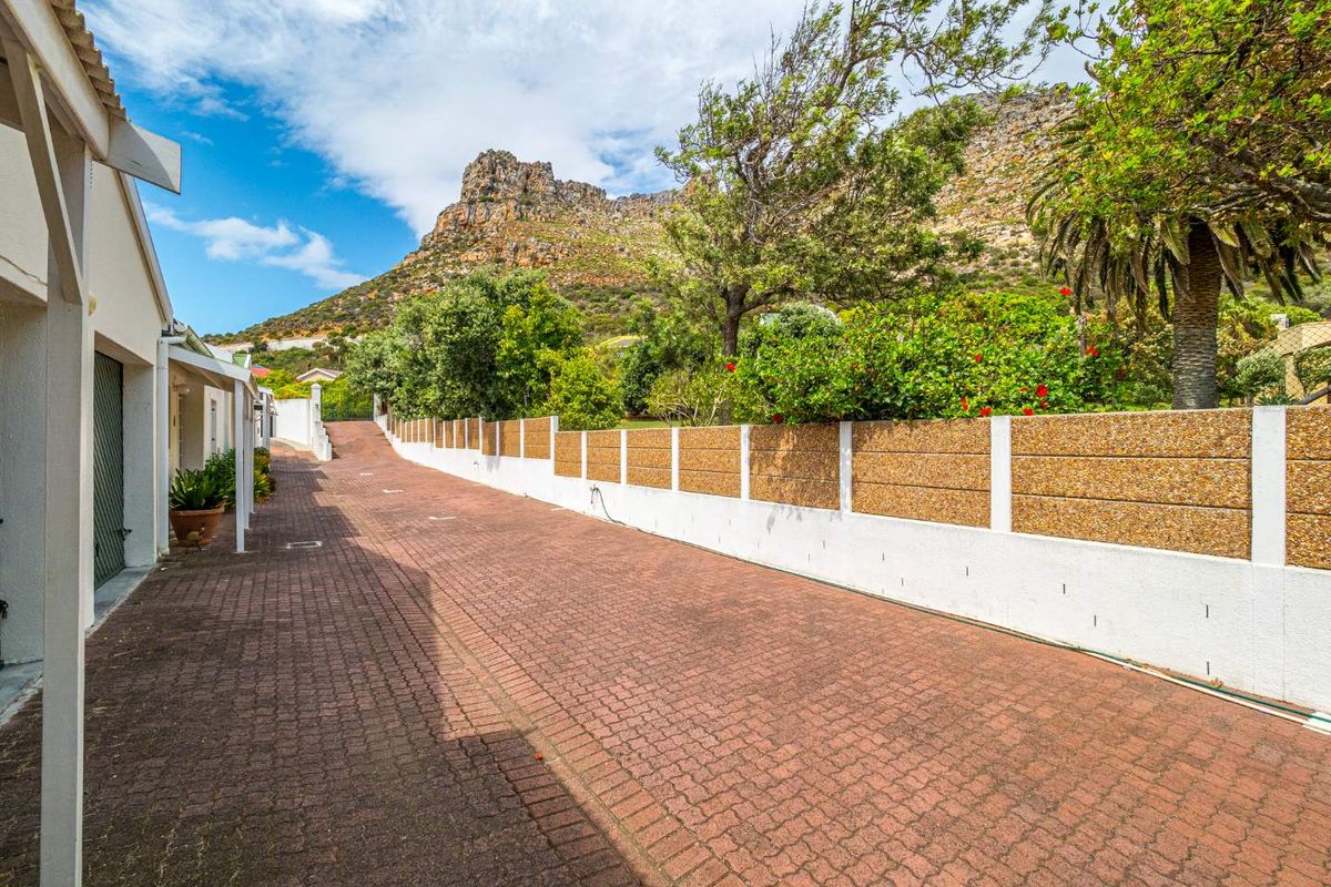 A paved driveway leading towards the townhouse garage, featuring a boundary wall and scenic mountain views in the background.