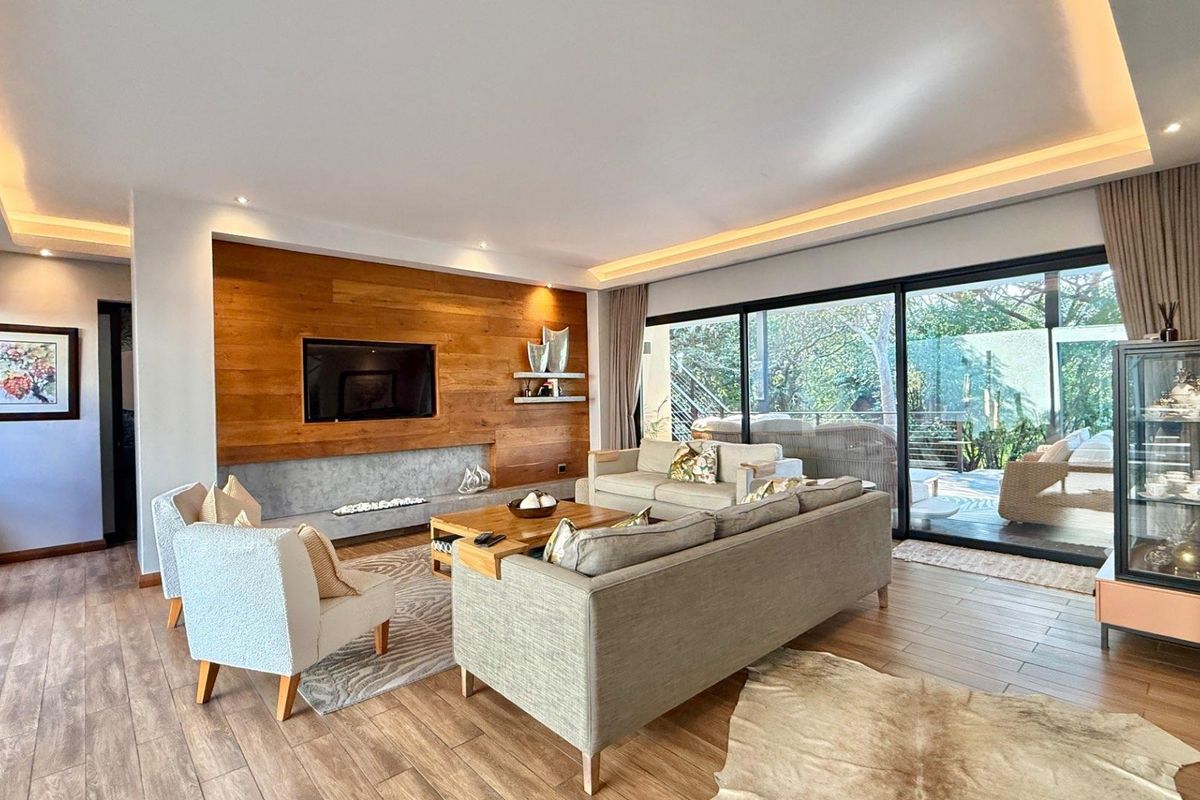 Spacious living room featuring wood-paneled accent wall, integrated fireplace, recessed cove lighting, and large sliding glass doors opening to an outdoor patio area.