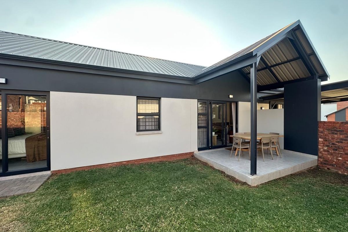 Rear view of the townhouse featuring a covered patio area, modern metal roofing, and sliding glass doors leading into the living space and garden.