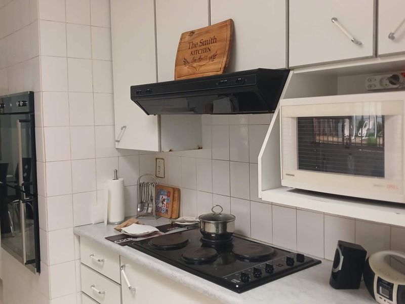A functional kitchen featuring white cabinetry, a built-in oven, electric hob, extractor fan, and a tiled splashback.