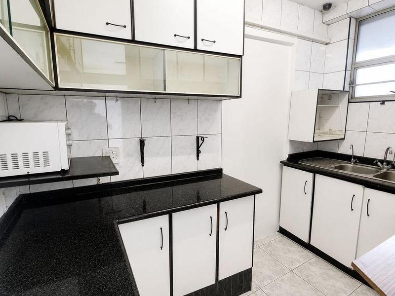 A functional kitchen featuring black granite countertops, white cabinetry with black trim, a double basin sink, and tiled finishes throughout.