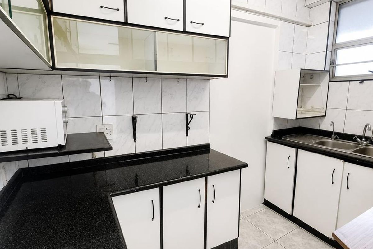 A functional kitchen featuring black granite countertops, white cabinetry with black trim, a double basin sink, and tiled finishes throughout.