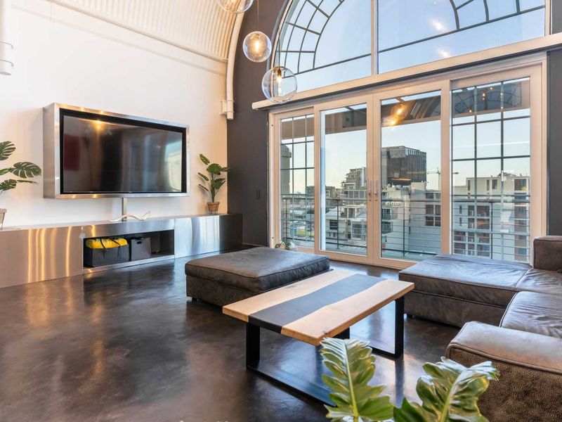 Modern living room featuring polished concrete floors, a vaulted ceiling, and a large arched window with city views and built-in media cabinetry.