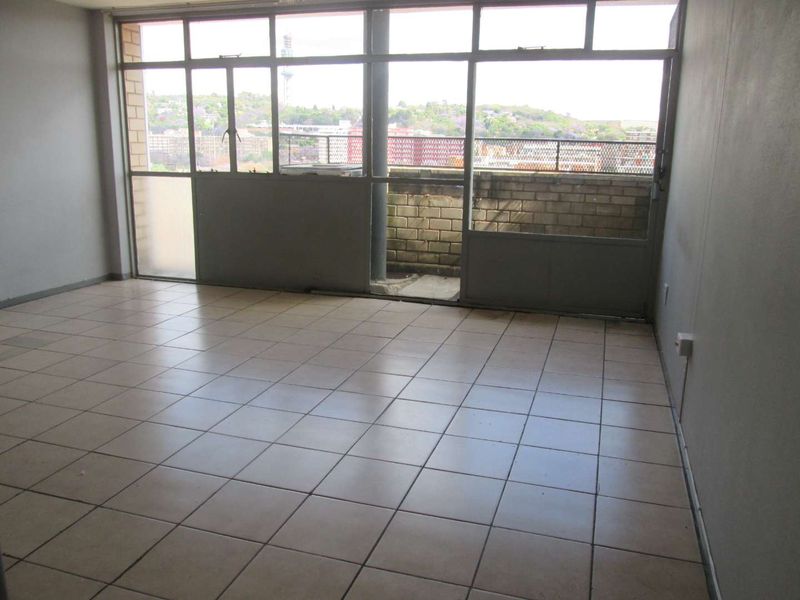 An empty living room featuring tiled flooring and large windows that provide natural light and access to an outdoor balcony area.