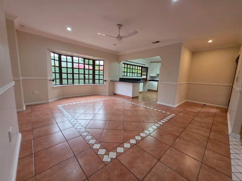 Spacious open-plan living and dining area featuring ceramic tile flooring, decorative molding, a ceiling fan, and a breakfast bar connecting to the kitchen.