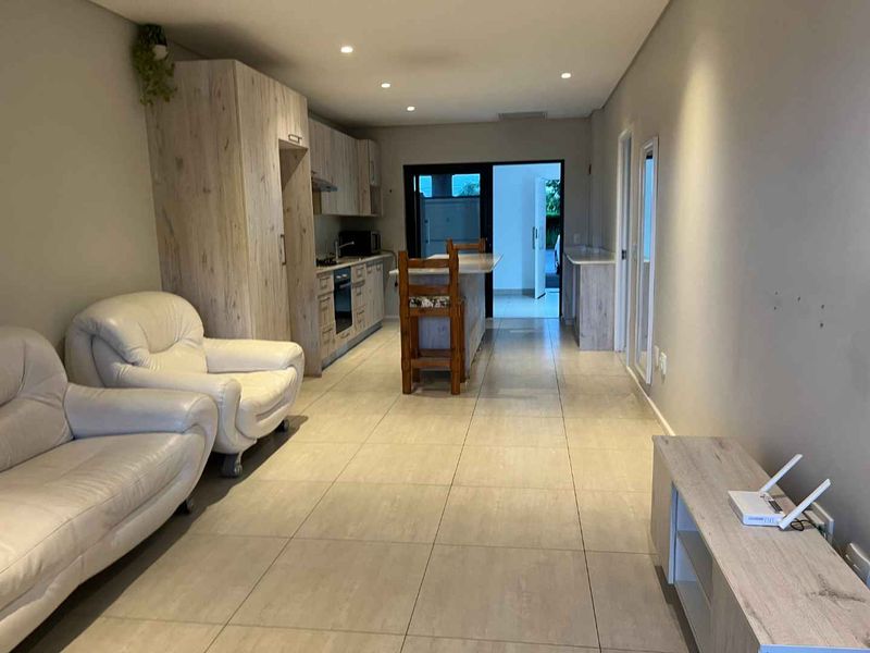 Open-plan living and kitchen area featuring modern wood-look cabinetry, a central island, tiled flooring, and direct access to an outdoor space.