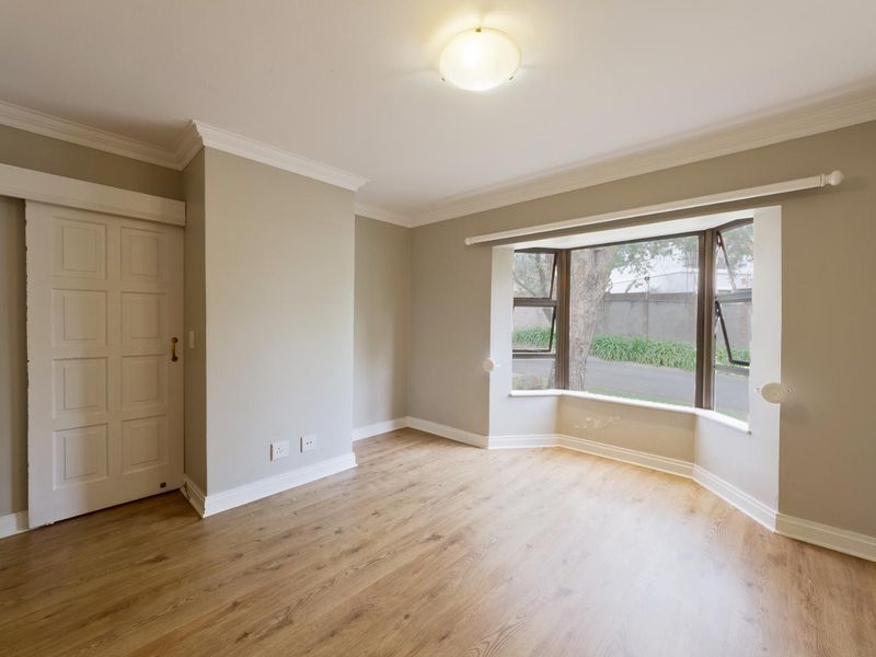 A bright, empty bedroom featuring laminate flooring, crown molding, and a large bay window providing natural light.