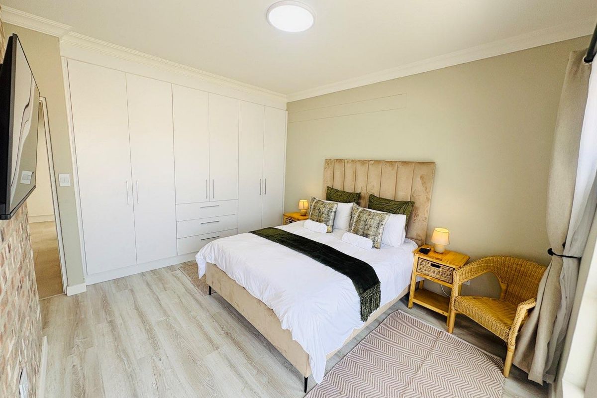 A well-maintained bedroom featuring light laminate flooring, neutral walls, and extensive built-in cupboard storage.