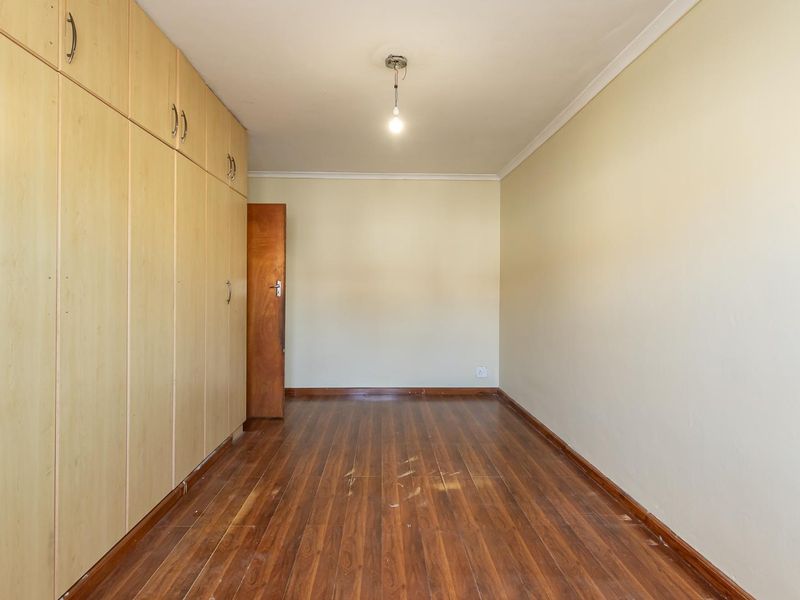 An empty bedroom featuring built-in wooden cupboards and laminate flooring, providing a blank canvas for potential interior design updates.