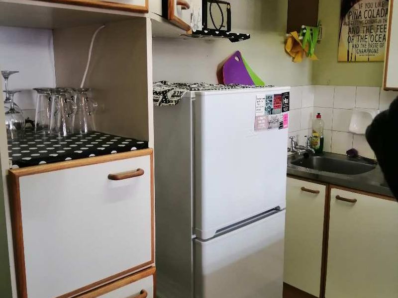 A compact kitchen featuring dated laminate cabinetry, a stainless steel sink, tiled backsplash, and tiled flooring, offering potential for a modern renovation.