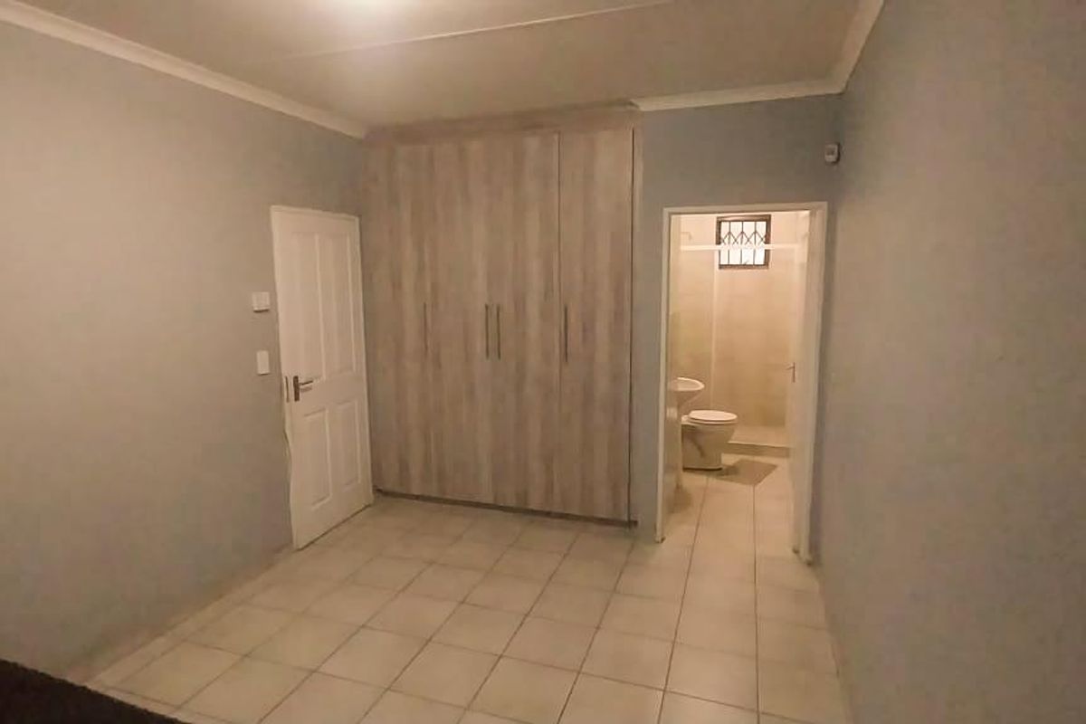 A bedroom featuring built-in wooden cupboards and an en-suite bathroom with tiled flooring throughout.