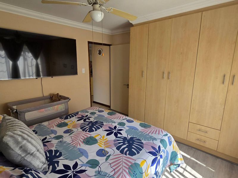 A bedroom featuring light wood-finish built-in cupboards, a ceiling fan, and neutral wall tones.