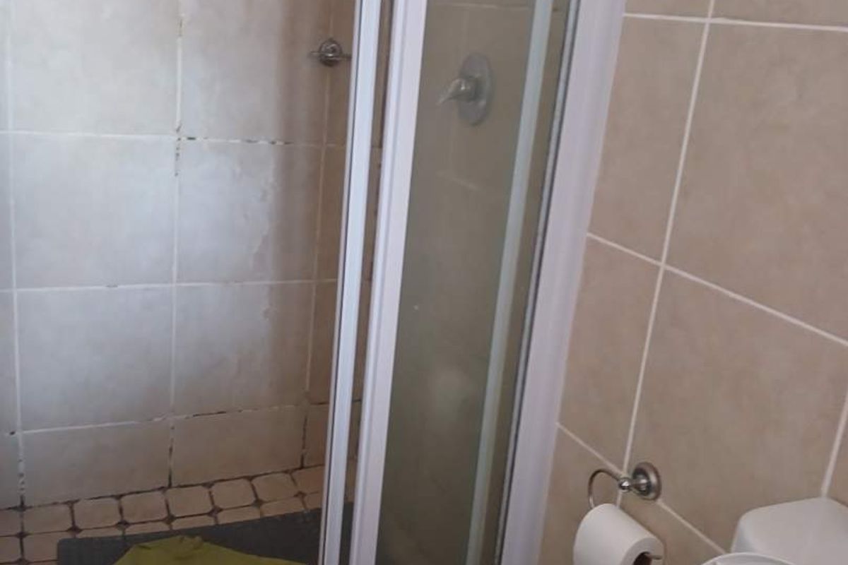 A compact bathroom featuring a tiled shower enclosure and a standard toilet, requiring maintenance and cosmetic updates to improve its overall condition.