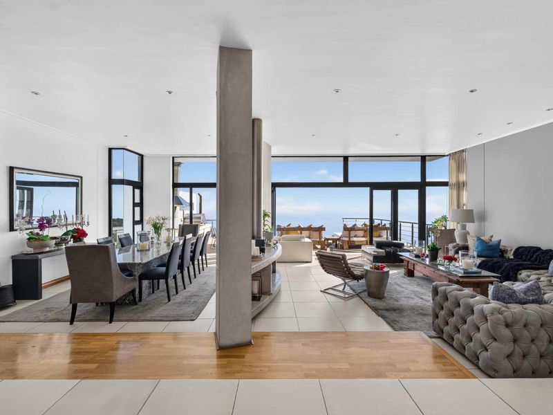 Spacious open-plan living and dining area featuring large format tiles, hardwood accents, and expansive floor-to-ceiling sliding doors opening to a scenic outdoor terrace.