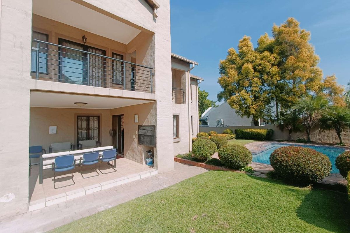Rear view of the property featuring a covered patio with a built-in braai, an upper balcony, a swimming pool, and a well-maintained garden.