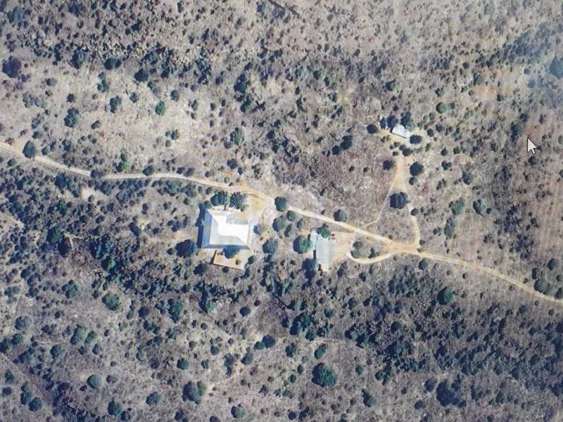An aerial view of a rural property featuring a main dwelling and outbuildings accessed by a dirt road in a natural landscape.