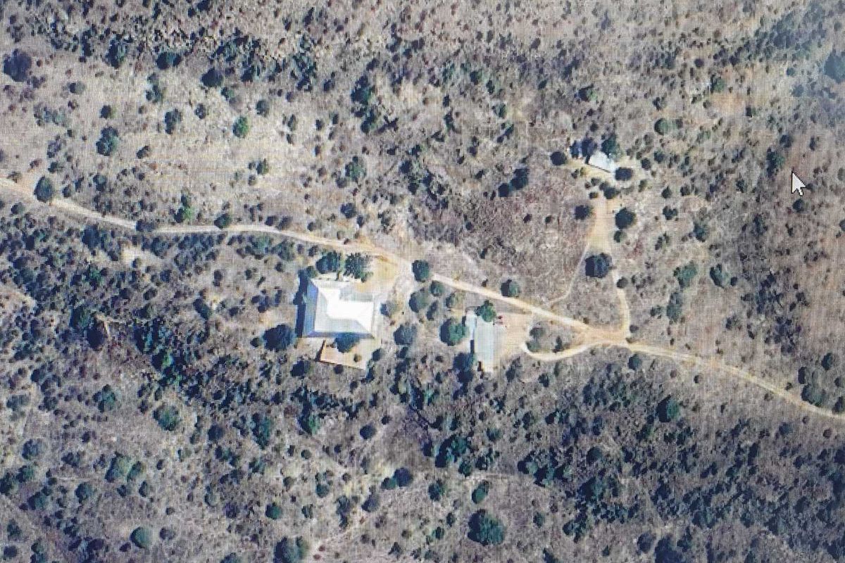 An aerial view of a rural property featuring a main dwelling and outbuildings accessed by a dirt road in a natural landscape.
