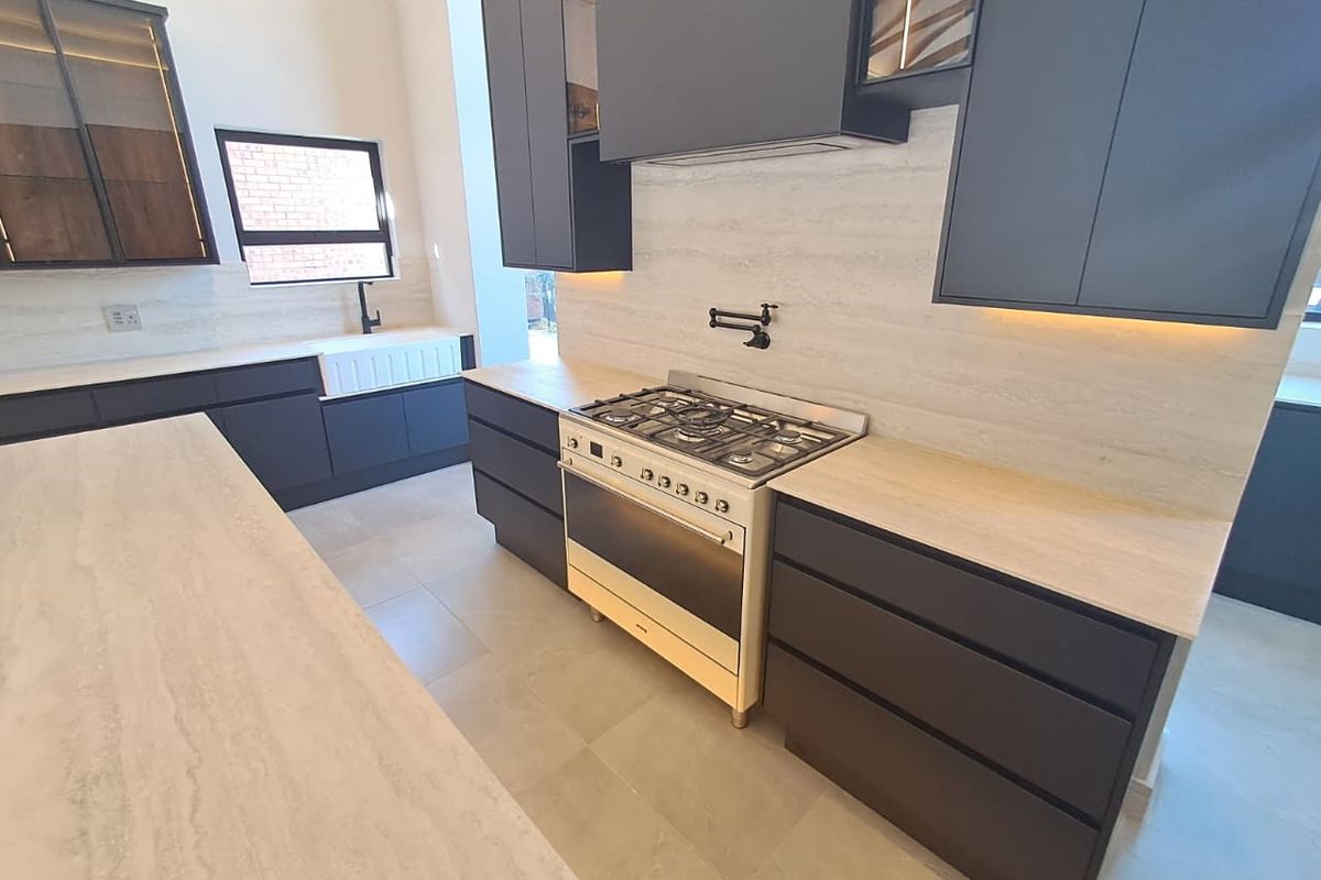 Modern kitchen featuring dark cabinetry, stone countertops, a gas stove with pot filler, and a farmhouse-style apron sink.