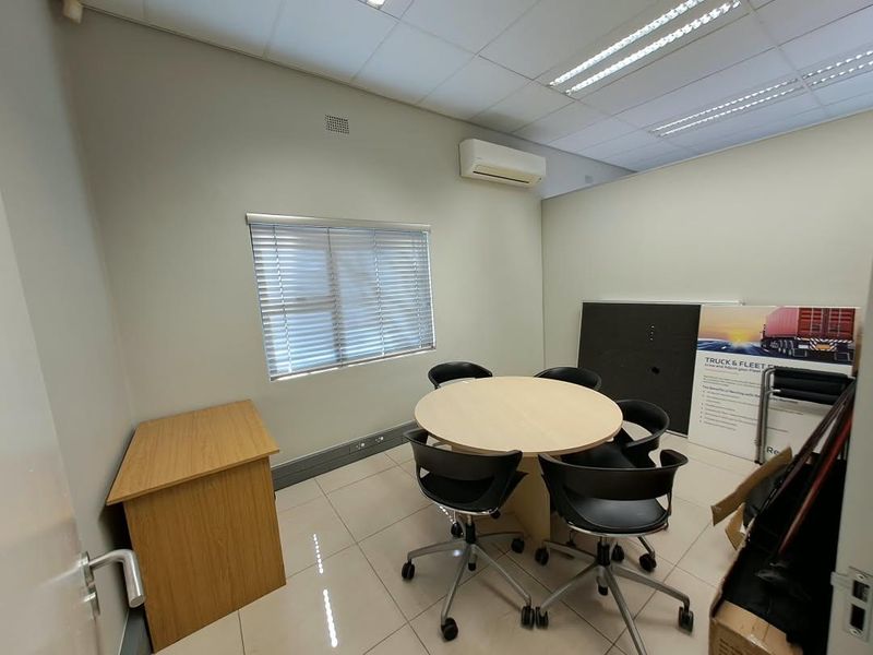 A functional office space featuring tiled flooring, a suspended ceiling with recessed lighting, and a wall-mounted air conditioning unit.