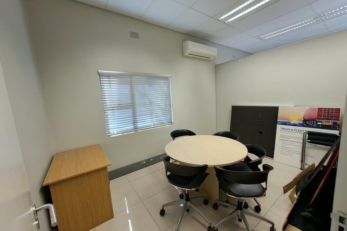 A functional office space featuring tiled flooring, a suspended ceiling with recessed lighting, and a wall-mounted air conditioning unit.