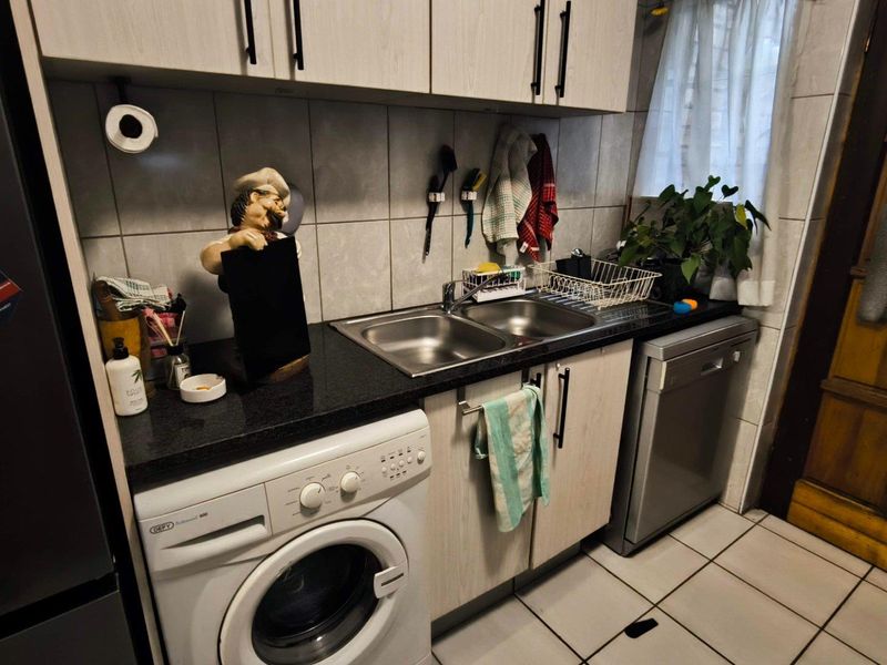 A functional scullery area featuring granite countertops, a double stainless steel sink, tiled backsplash, and built-in cabinetry with space for laundry appliances.