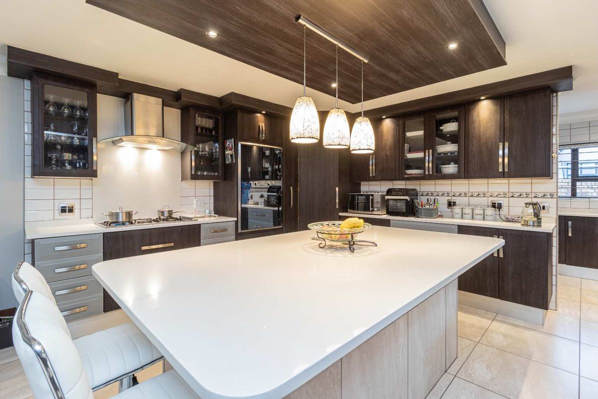 Modern kitchen featuring dark wood cabinetry, a large central island with stone countertop, integrated appliances, and stylish pendant lighting.
