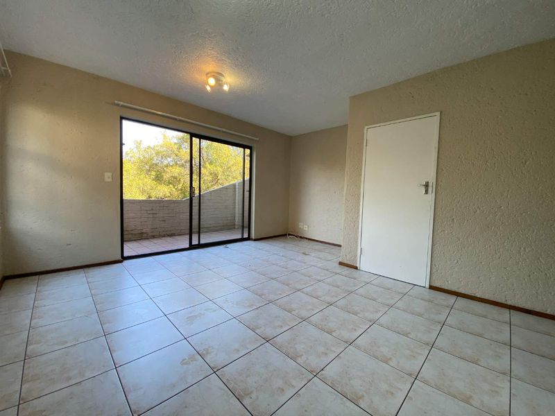 An empty living room featuring ceramic tiled flooring, textured walls, and a sliding glass door providing access to an outdoor patio area.