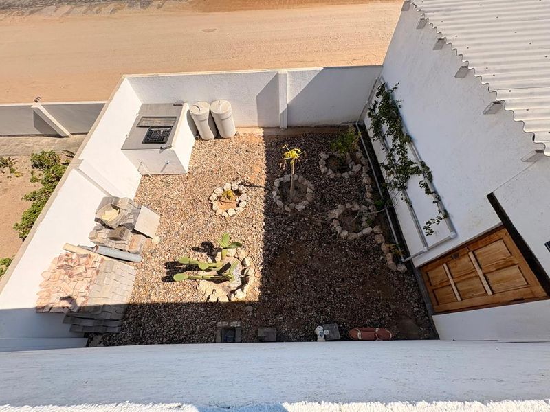 An elevated view of a rear courtyard featuring a built-in braai, gravel landscaping, and perimeter walls, currently requiring some finishing and tidying.