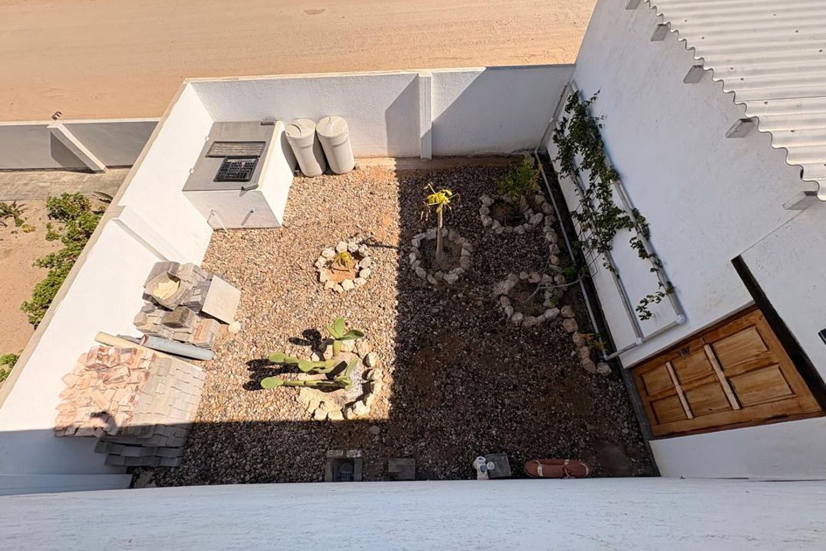 An elevated view of a rear courtyard featuring a built-in braai, gravel landscaping, and perimeter walls, currently requiring some finishing and tidying.