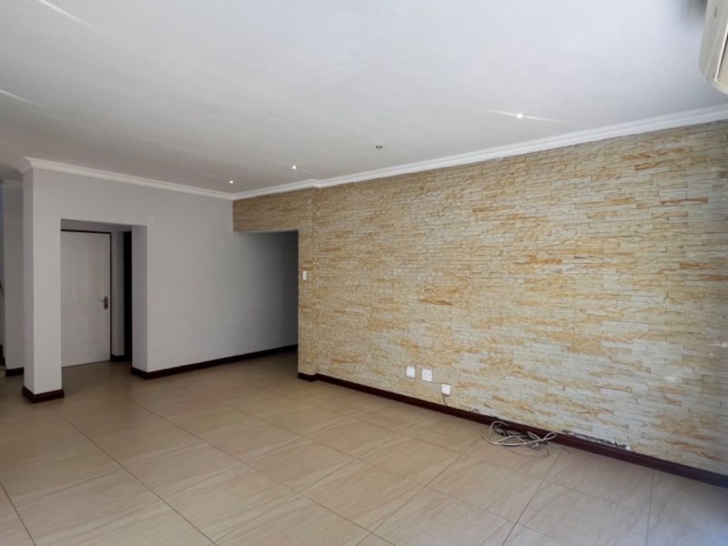 Spacious living area featuring a textured stone feature wall, neutral tiled flooring, recessed lighting, and an integrated air conditioning unit.