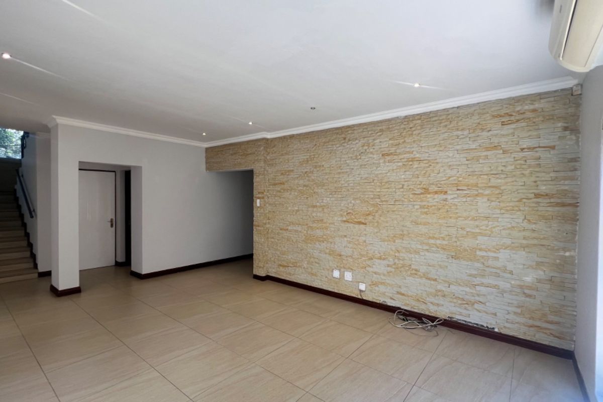 Spacious living area featuring a textured stone feature wall, neutral tiled flooring, recessed lighting, and an integrated air conditioning unit.