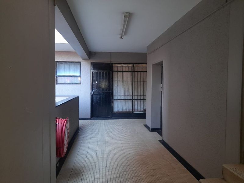 A communal apartment hallway featuring tiled flooring, a fire hose reel, and security gates leading to residential units.