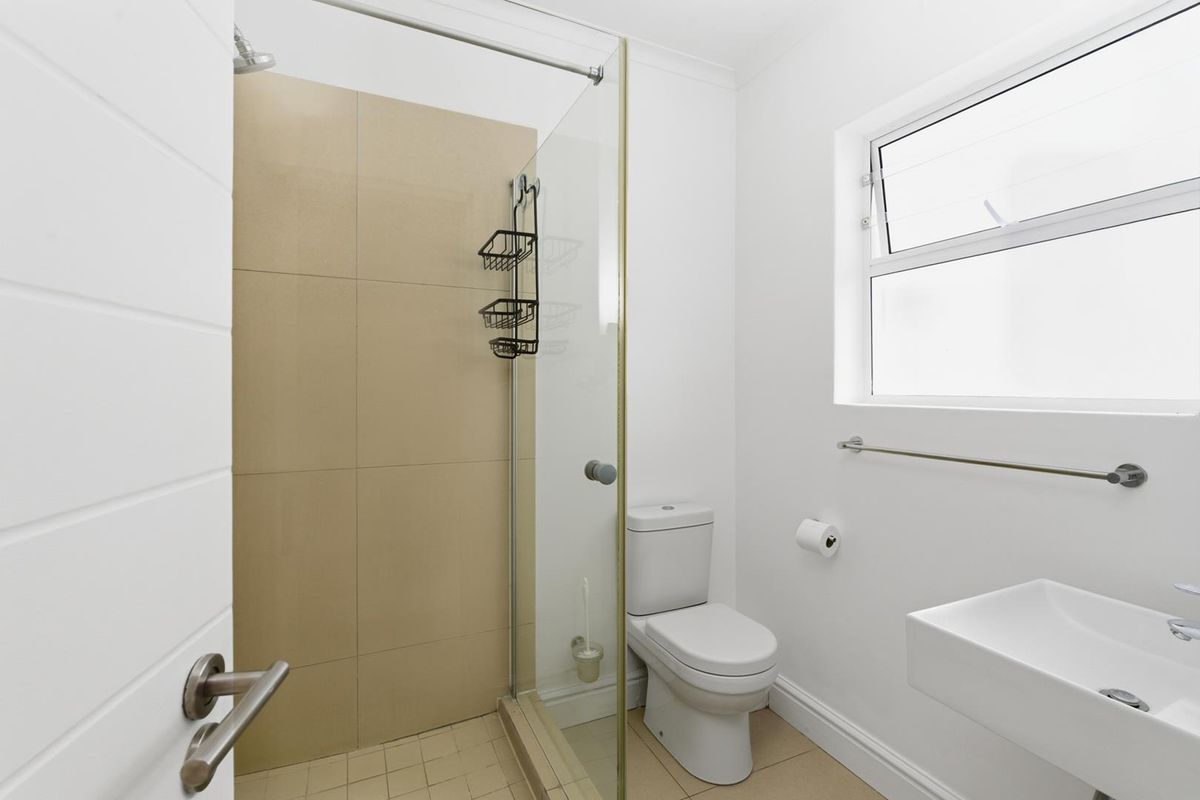 A clean, modern bathroom featuring a glass-enclosed shower, a wall-mounted basin, and a toilet, finished with neutral wall and floor tiles.