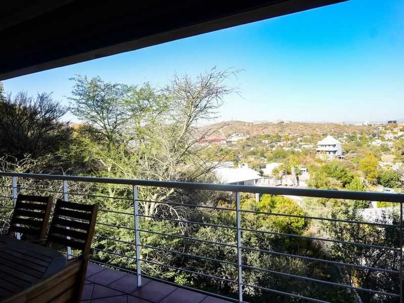A covered balcony featuring tiled flooring and a metal balustrade, offering expansive elevated views of the surrounding landscape and neighborhood.