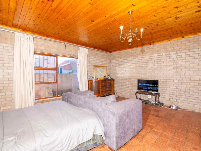 Spacious bedroom featuring exposed brick walls, a timber tongue and groove ceiling, and tiled flooring, offering a rustic aesthetic.