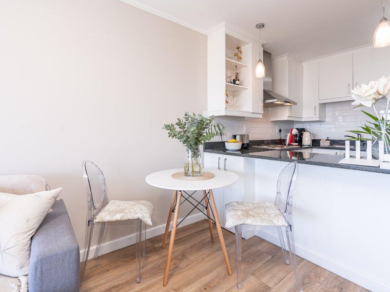 An open-plan kitchen and dining area featuring white cabinetry, granite countertops, subway tile backsplash, and modern laminate flooring.