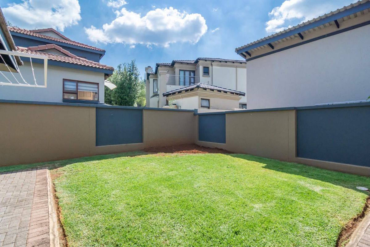 A private rear garden featuring a manicured lawn, paved walkway, and high perimeter boundary walls, offering a secure outdoor space.