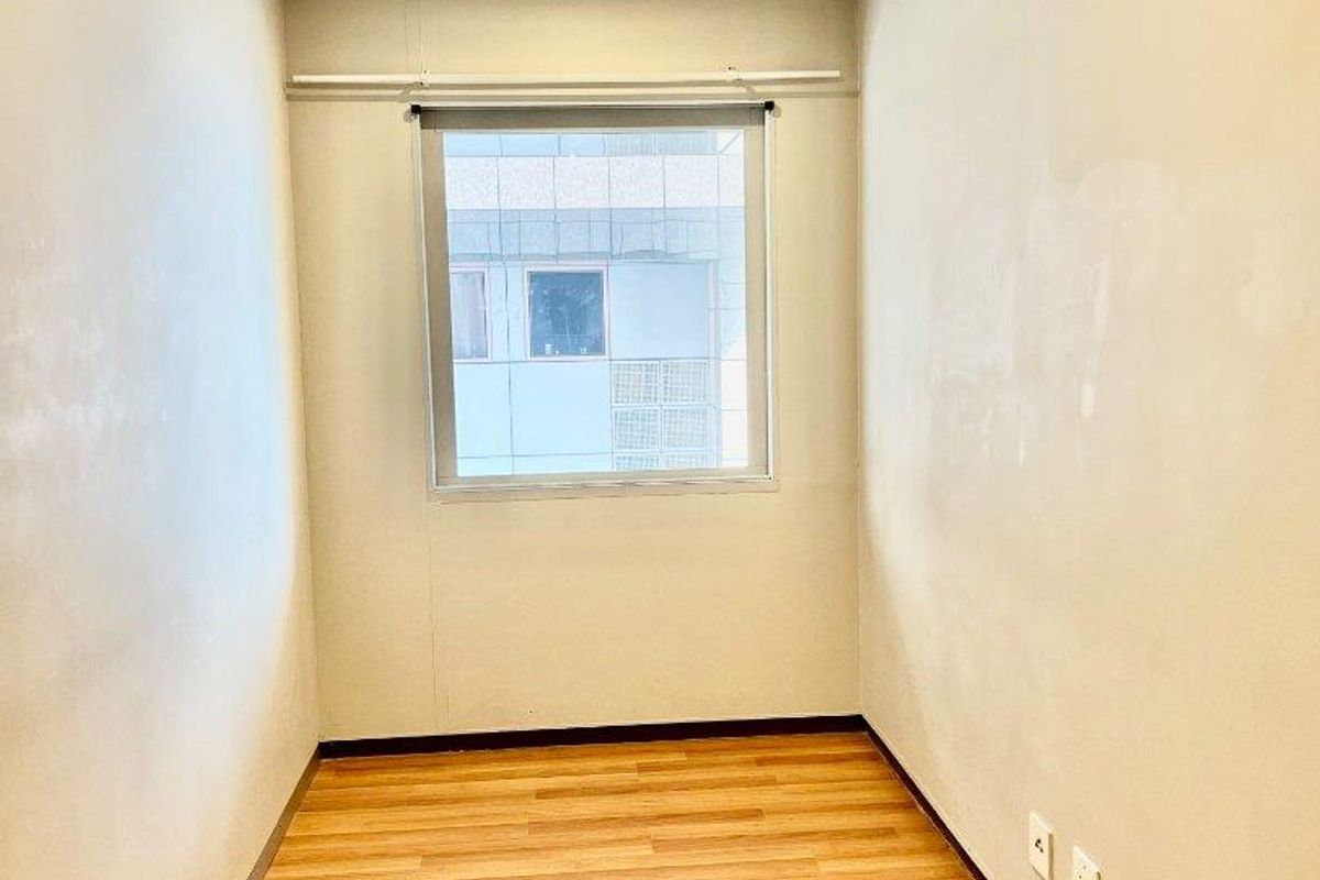 An empty bedroom featuring laminate flooring, a drop ceiling, and a window, providing a blank canvas for potential interior design and staging.