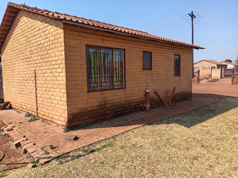 Rear view of a single-story clay brick house featuring a tiled roof, paved walkway, and security-fitted windows.