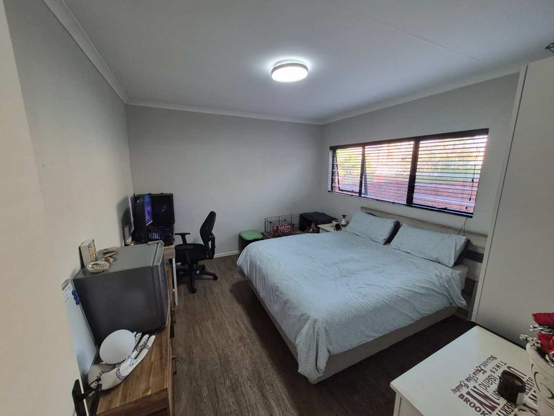 A well-maintained bedroom featuring laminate flooring, neutral wall finishes, and horizontal window blinds providing natural light.