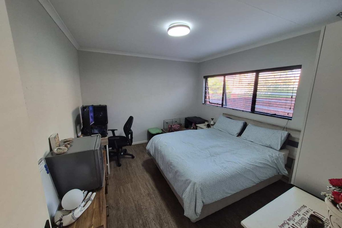 A well-maintained bedroom featuring laminate flooring, neutral wall finishes, and horizontal window blinds providing natural light.