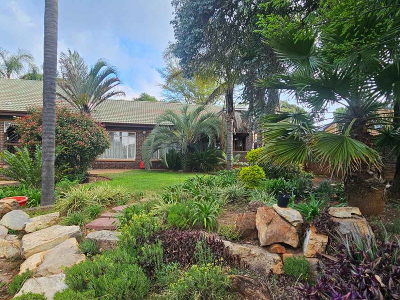 A well-maintained rear garden featuring a landscaped rockery, mature trees, and a brick-faced house with a tiled roof.