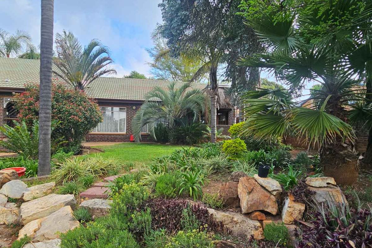 A well-maintained rear garden featuring a landscaped rockery, mature trees, and a brick-faced house with a tiled roof.