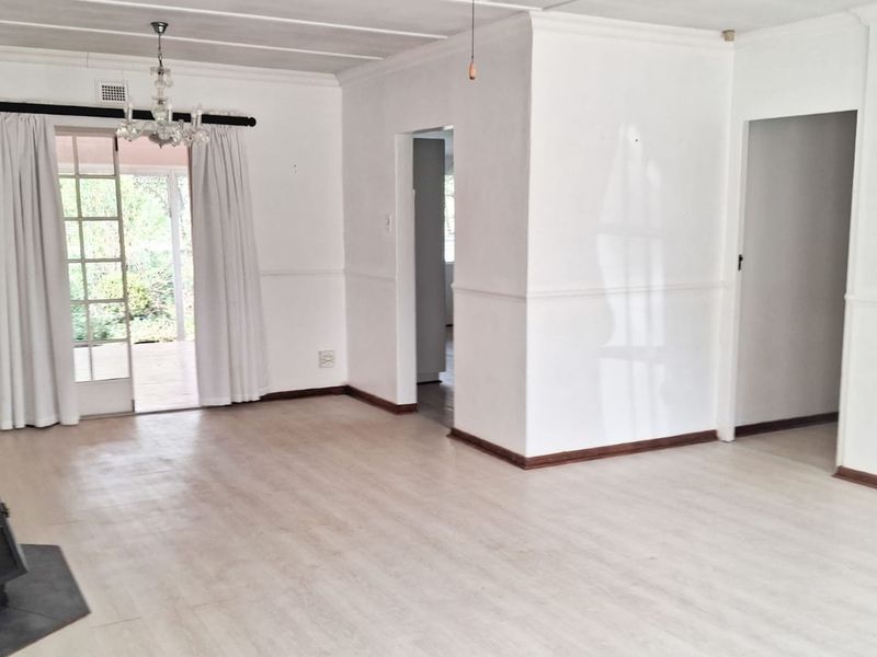 Spacious, empty living room featuring light laminate flooring, a freestanding fireplace, and direct access to the garden through glass french doors.